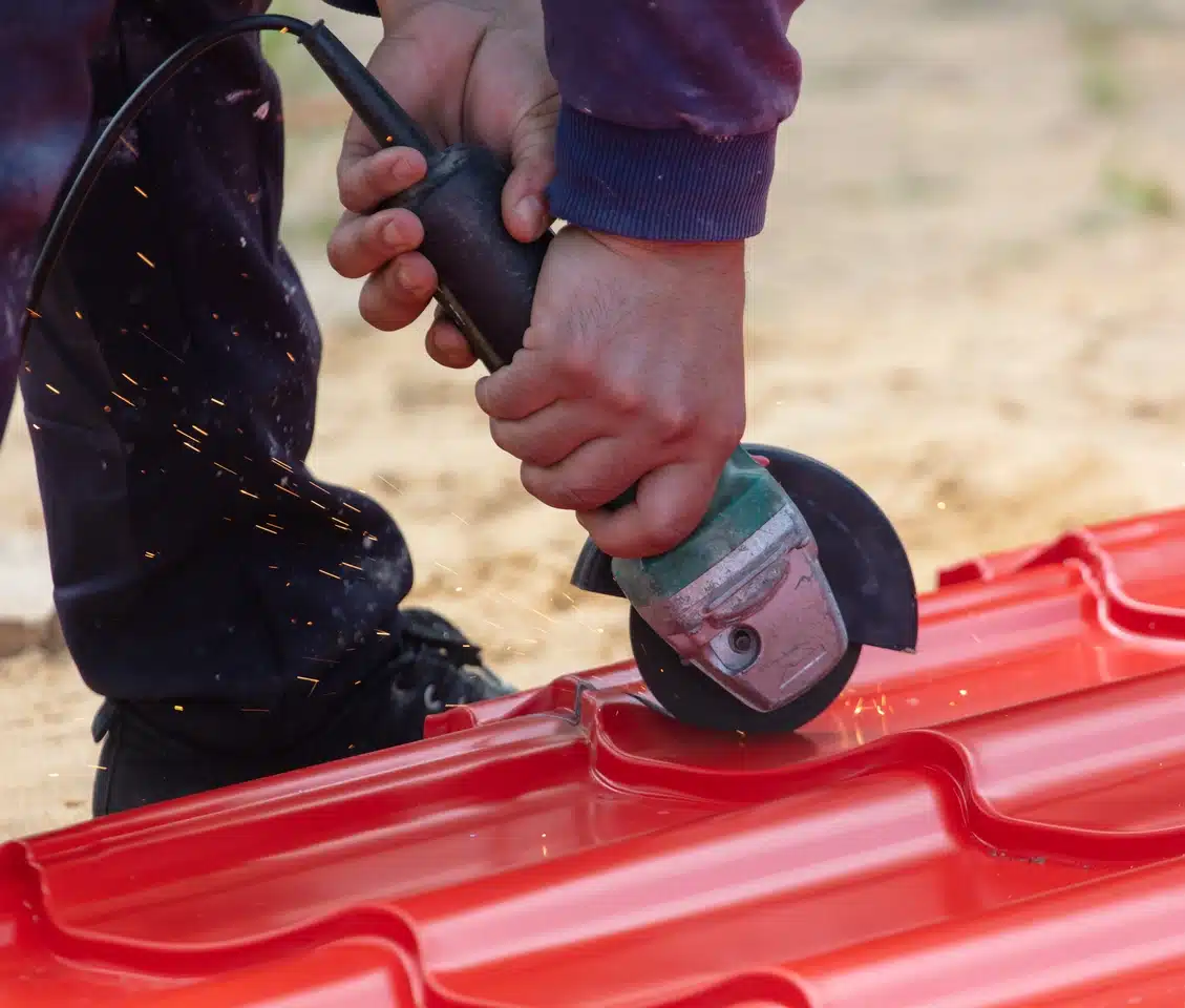 man using drill to cut red metal roofing sheet