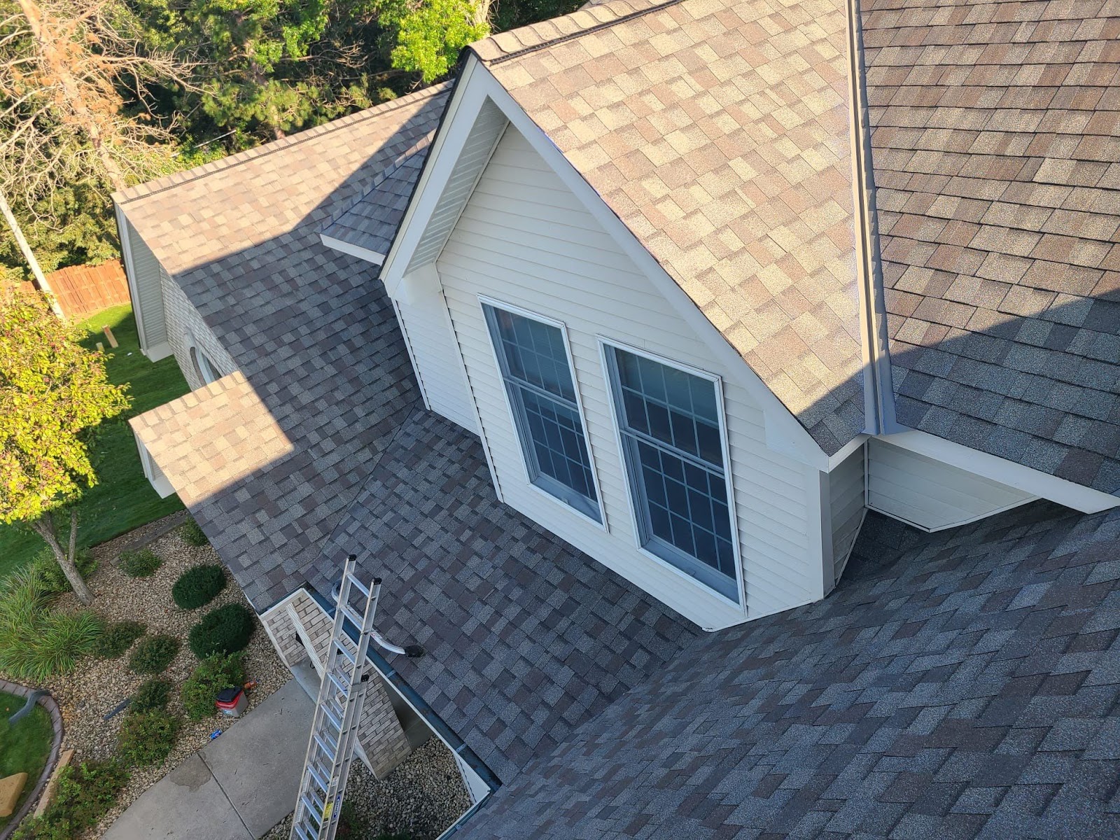 Elevated view of a completed gray shingle roof around a white dormer