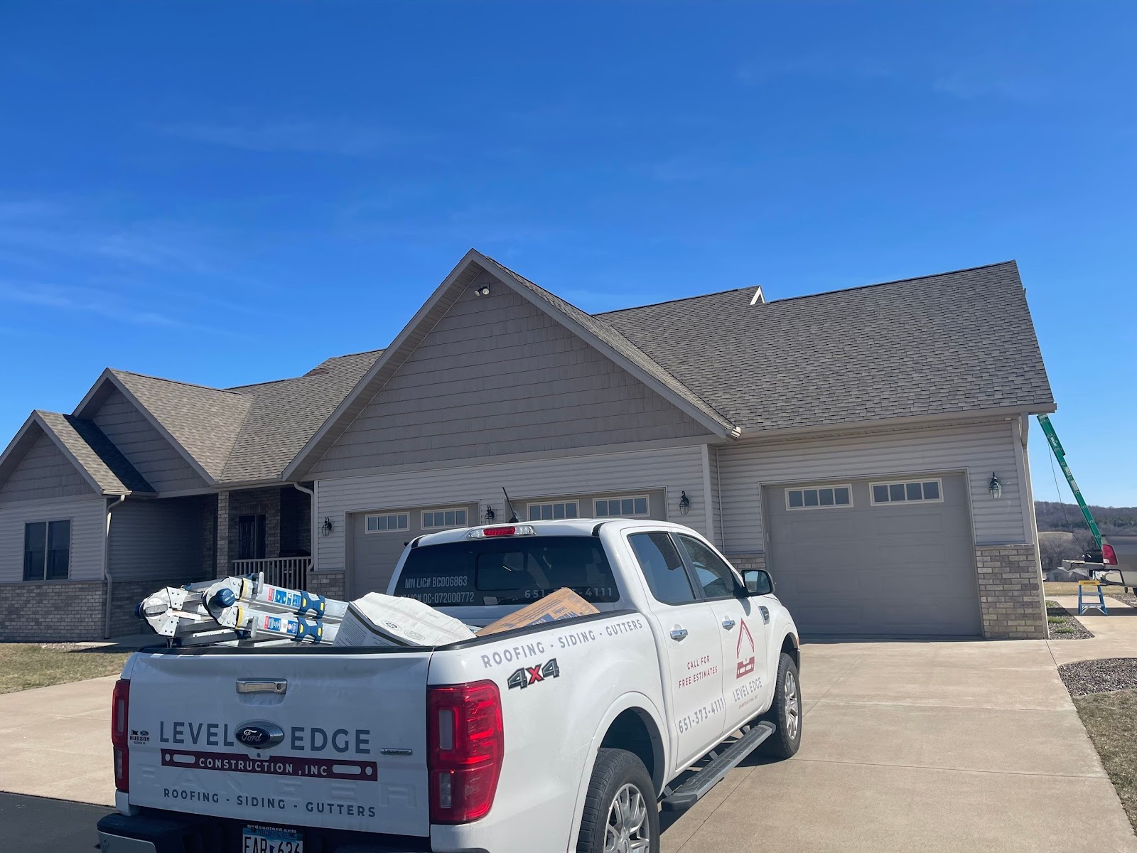Completed gray shingle gable roof above a two-car garage with a Level Edge truck in front