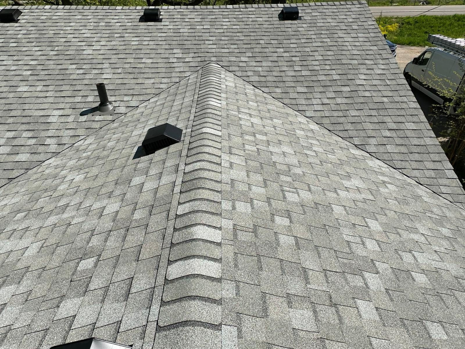 Close view of finished gray shingles, hip ridge caps, and roof vents
