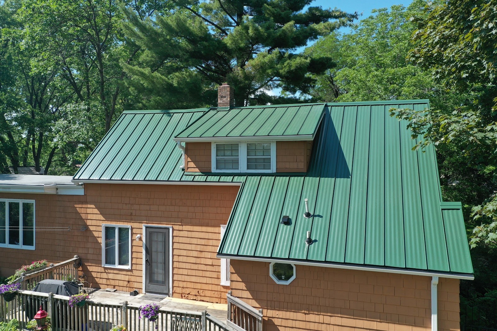 Green standing-seam metal roof with a dormer on a tan house