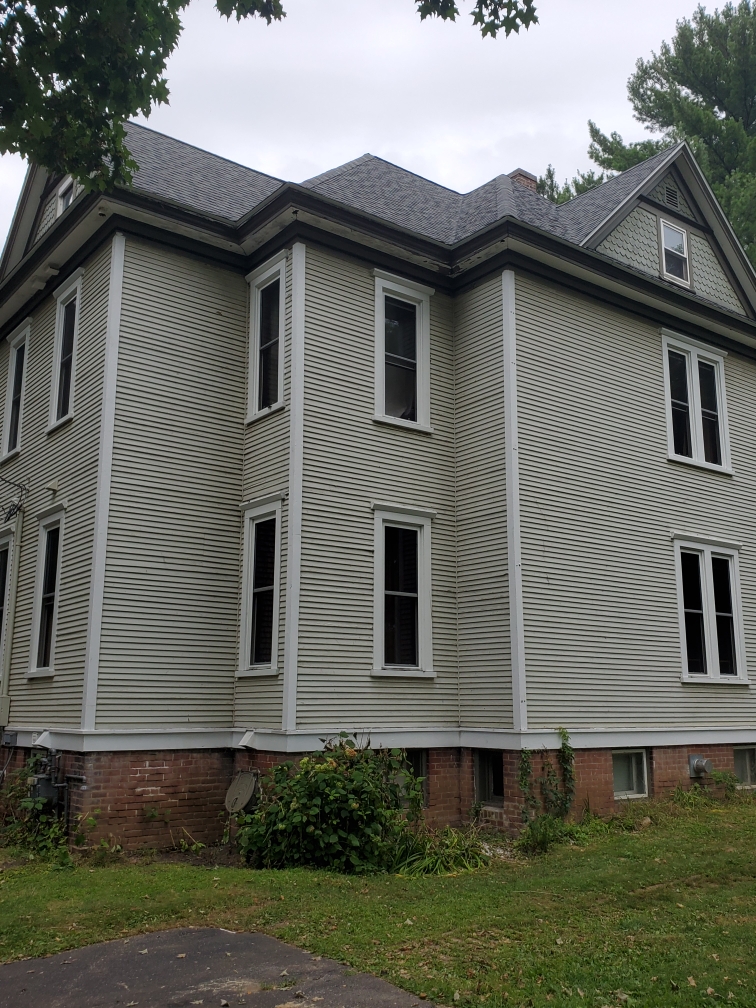 Dark shingle roofline above a two-story light-sided home with projecting bays