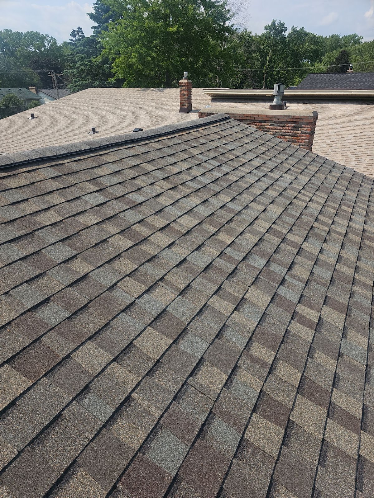 Finished shingle roof viewed toward a brick chimney and adjoining roof planes