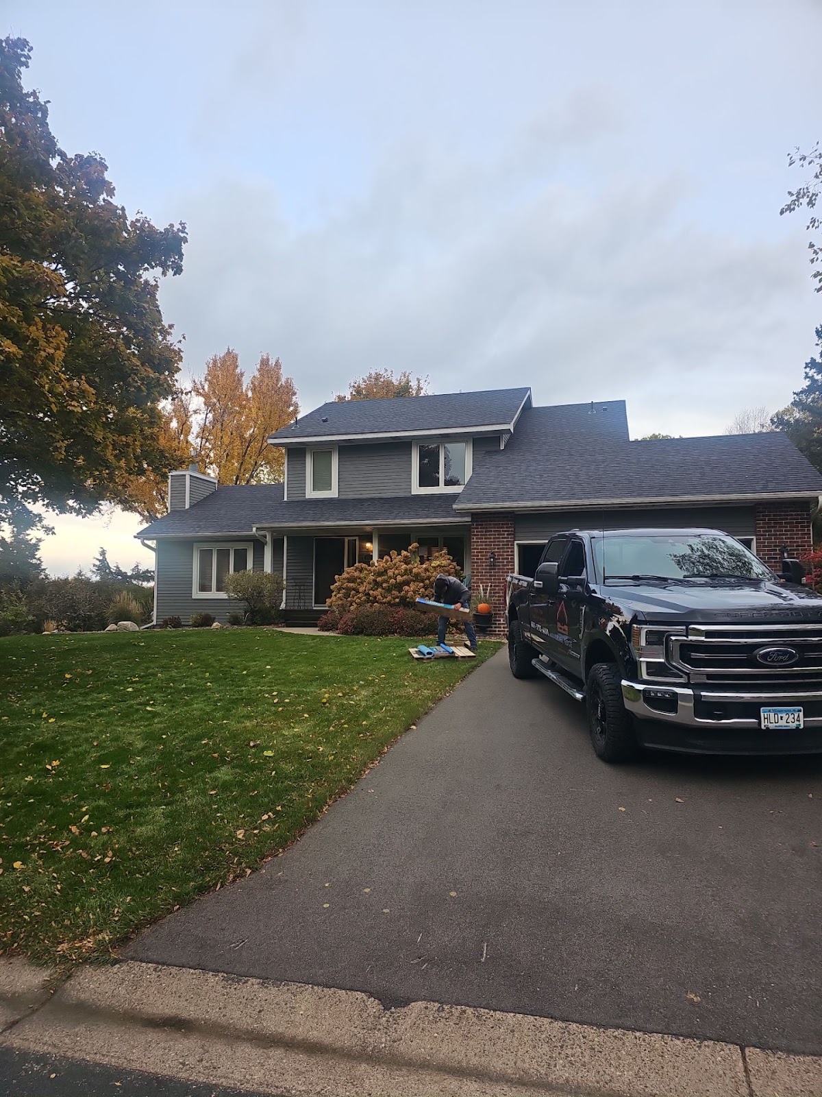 Completed shingle roof on a two-story home beside autumn trees
